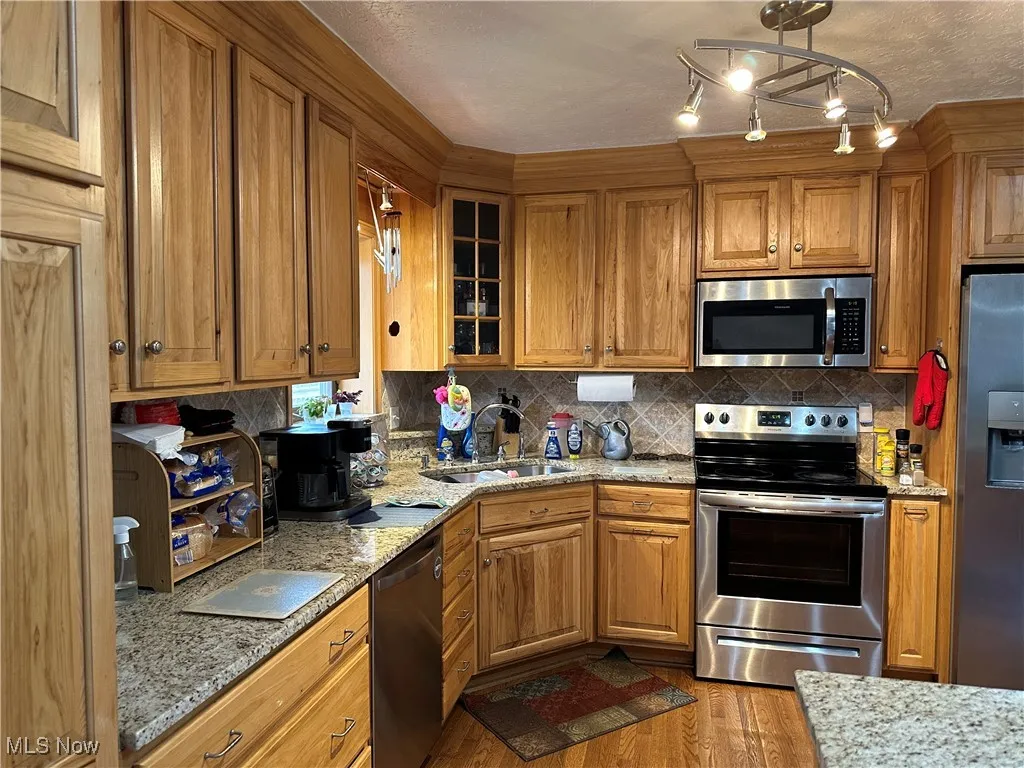Kitchen featuring a sink, wood finished floors, brown cabinetry, stainless steel appliances, and decorative backsplash