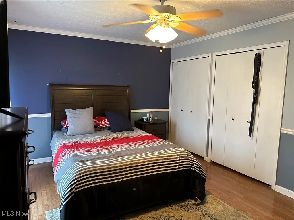 Bedroom with ornamental molding, a textured ceiling, multiple closets, and wood finished floors