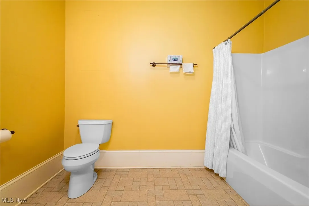 Bathroom with toilet, tile flooring, and shower / tub combo with curtain