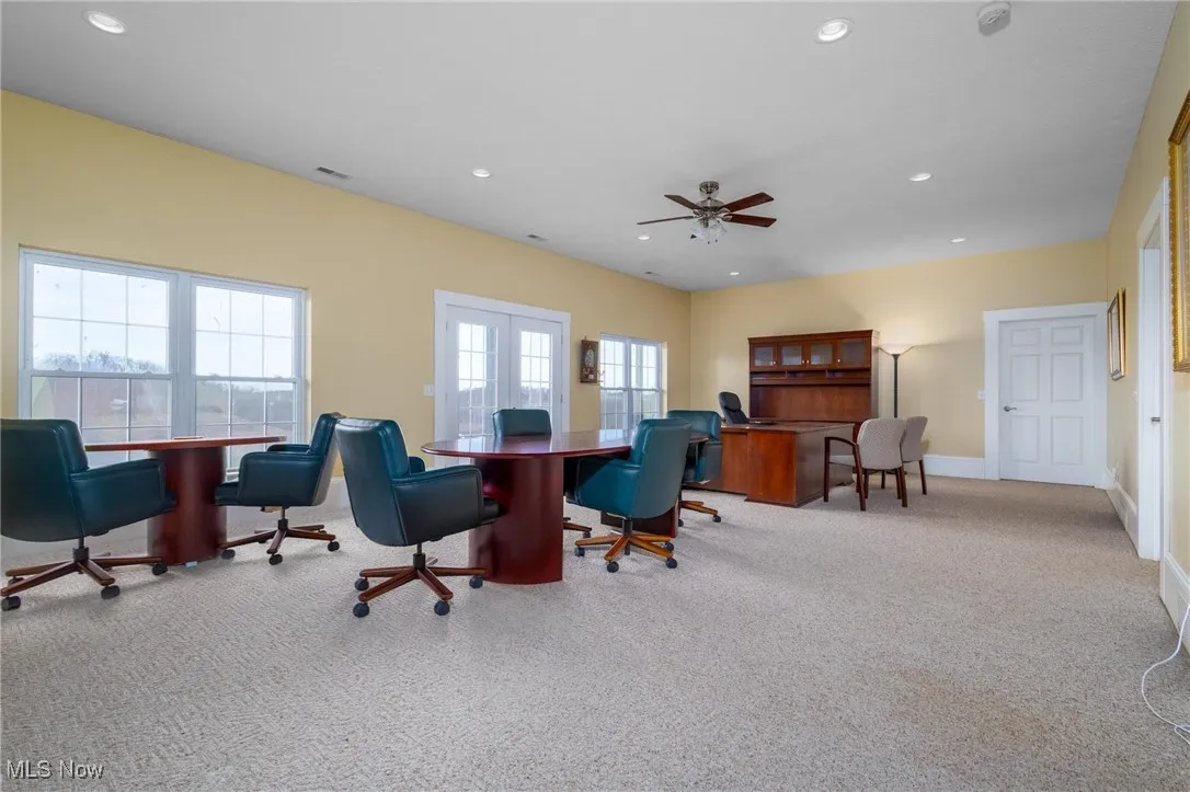 Office space featuring a healthy amount of sunlight, light carpet, ceiling fan, and french doors