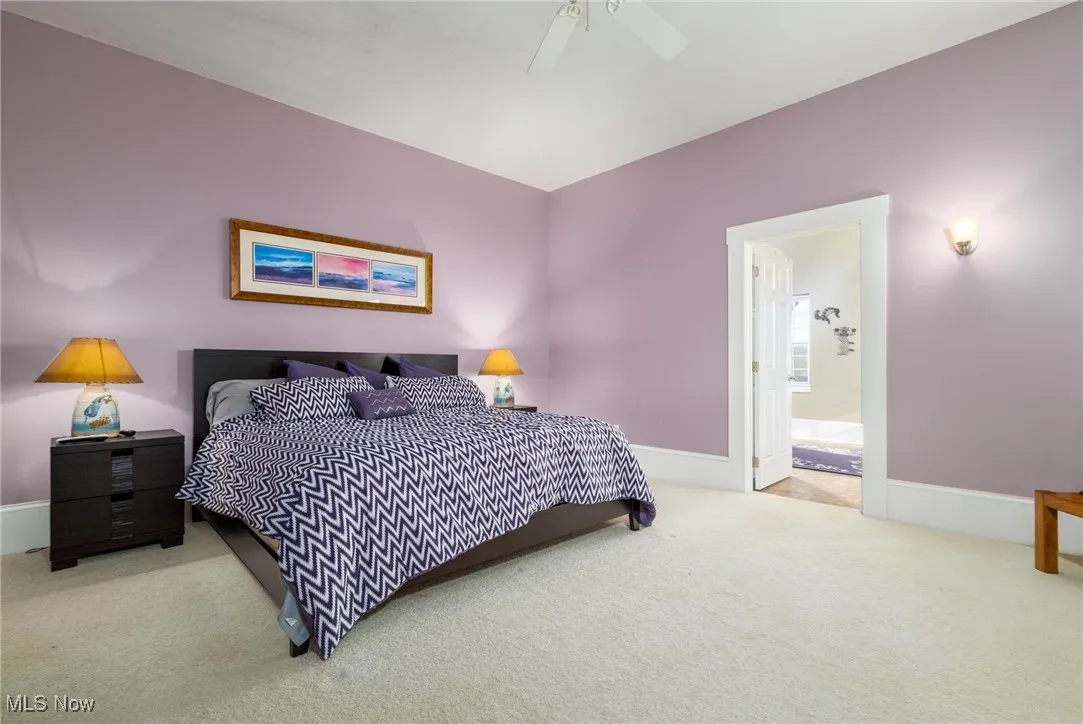 Bedroom with ensuite bathroom, light colored carpet, and ceiling fan
