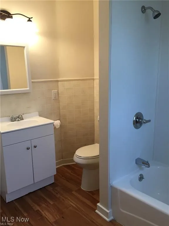 Full bathroom featuring vanity, tile walls, toilet, bathtub / shower combination, and wood finished floors