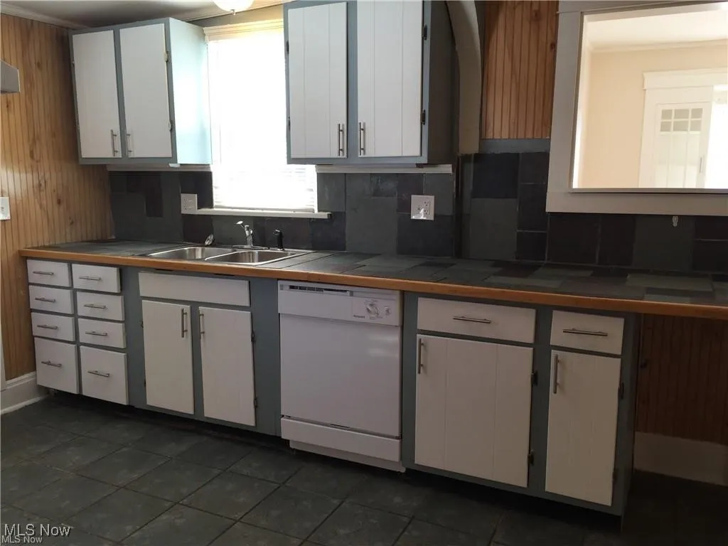 Kitchen featuring backsplash, a sink, tile counters, white cabinetry, and white dishwasher