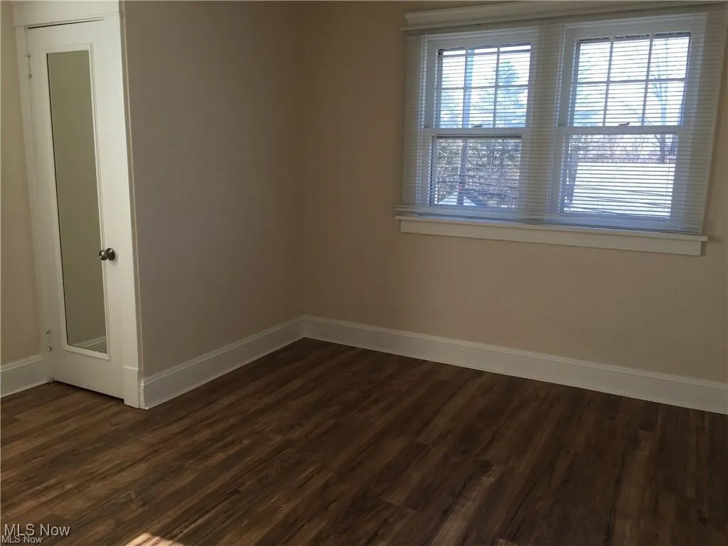 Empty room with baseboards and dark wood-type flooring