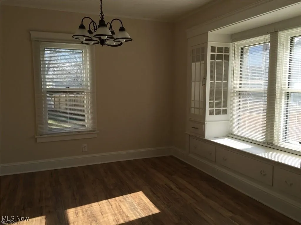 Unfurnished dining area with ornamental molding, a notable chandelier, dark wood-style floors, and baseboards