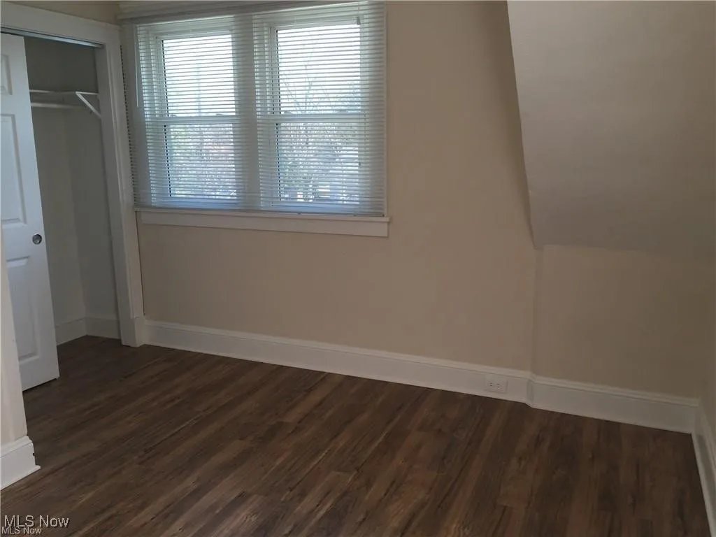 Unfurnished bedroom featuring dark wood-style flooring, a closet, and baseboards