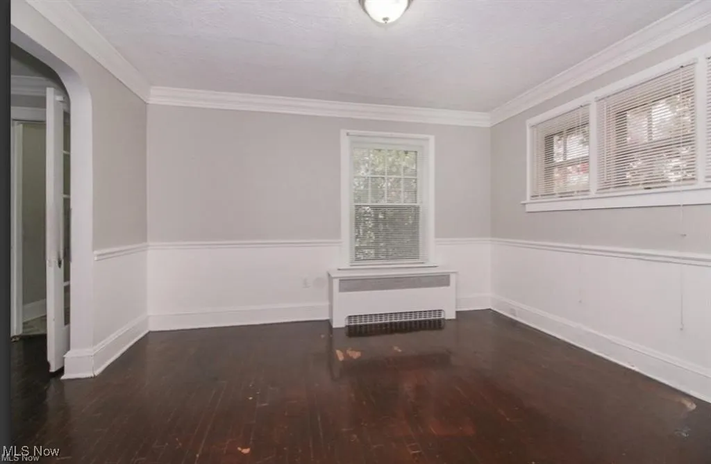 Unfurnished room with crown molding, wood finished floors, radiator, wainscoting, and arched walkways