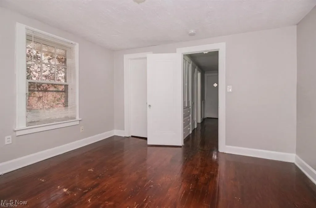 Empty room with a textured ceiling, baseboards, and wood finished floors