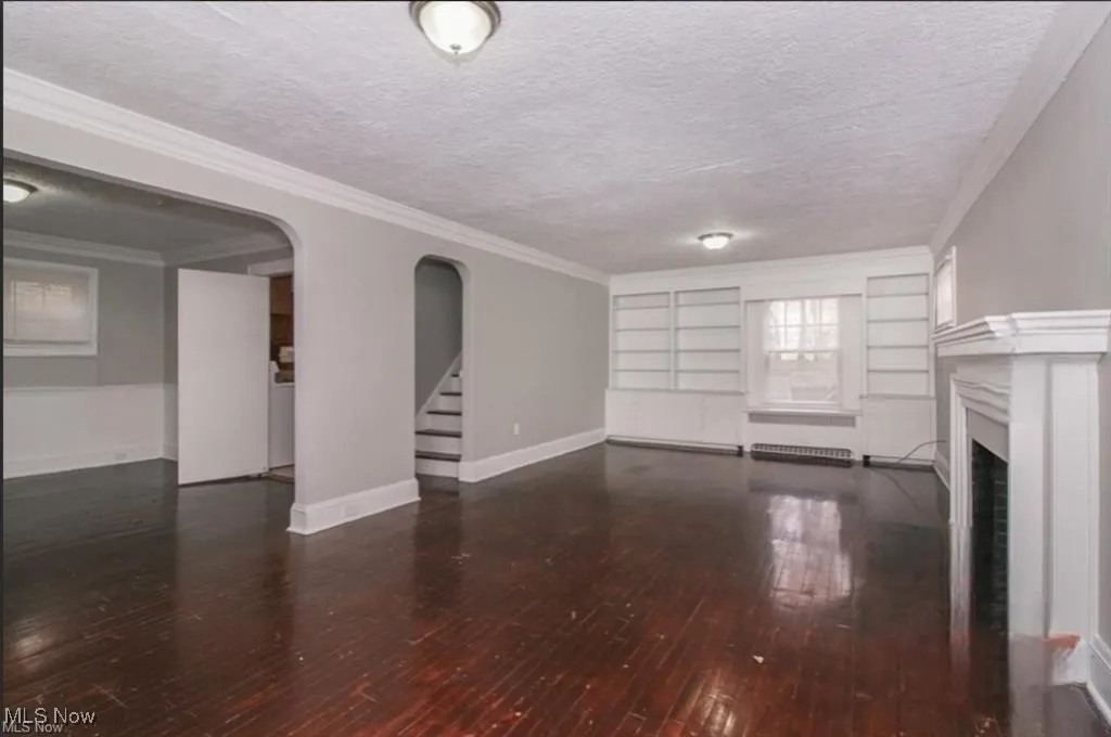 Unfurnished living room featuring stairs, crown molding, a fireplace, a textured ceiling, and wood-type flooring