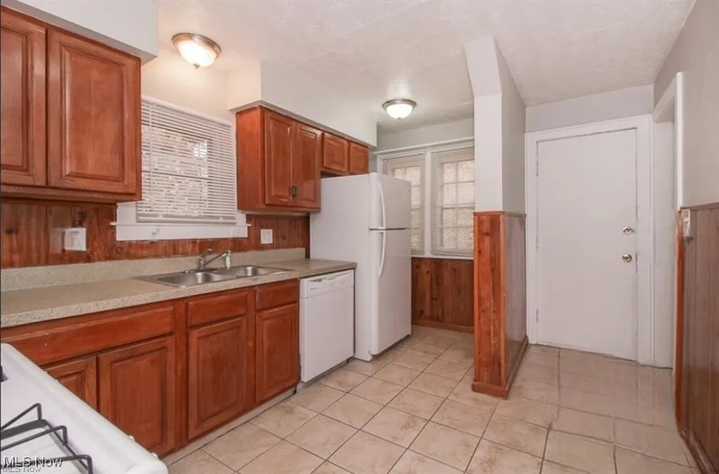 Kitchen with light countertops, white appliances, a sink, wooden walls, and brown cabinetry