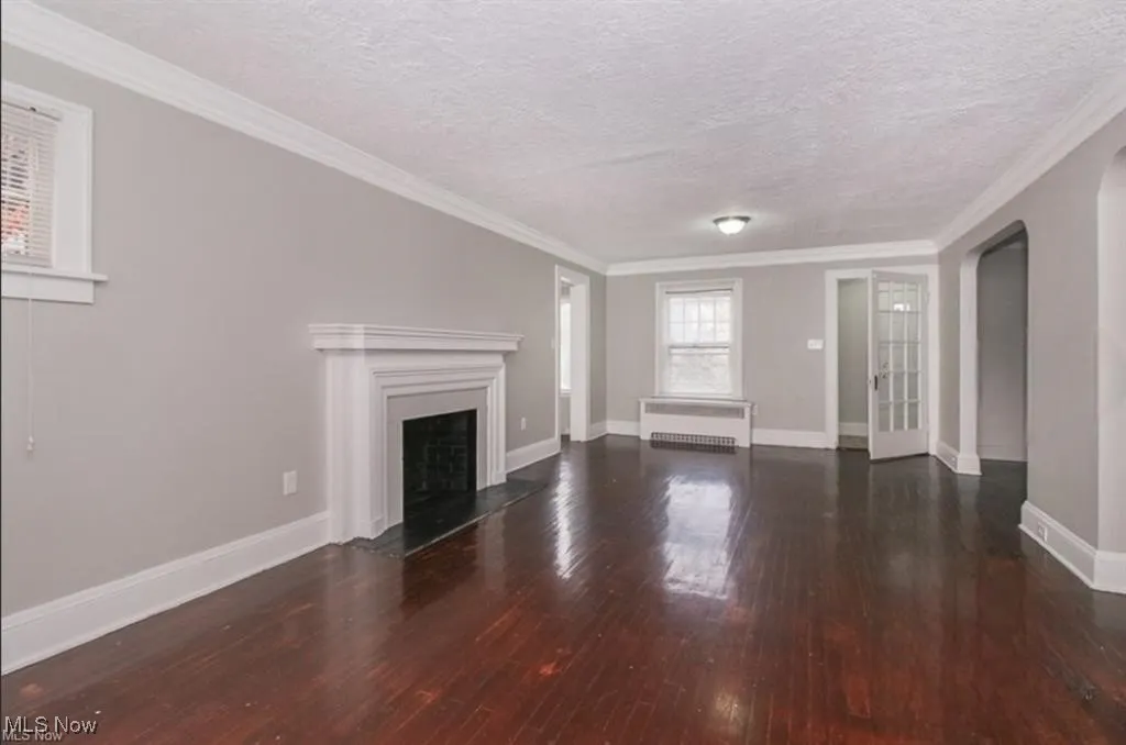 Unfurnished living room featuring hardwood / wood-style floors, ornamental molding, baseboards, a textured ceiling, and radiator heating unit