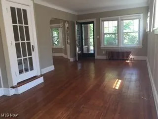 Unfurnished room featuring wood finished floors, radiator heating unit, baseboards, arched walkways, and ornamental molding