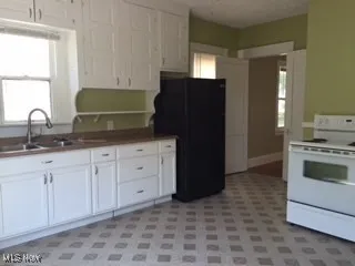 Kitchen with white cabinets, white electric range oven, a sink, and freestanding refrigerator