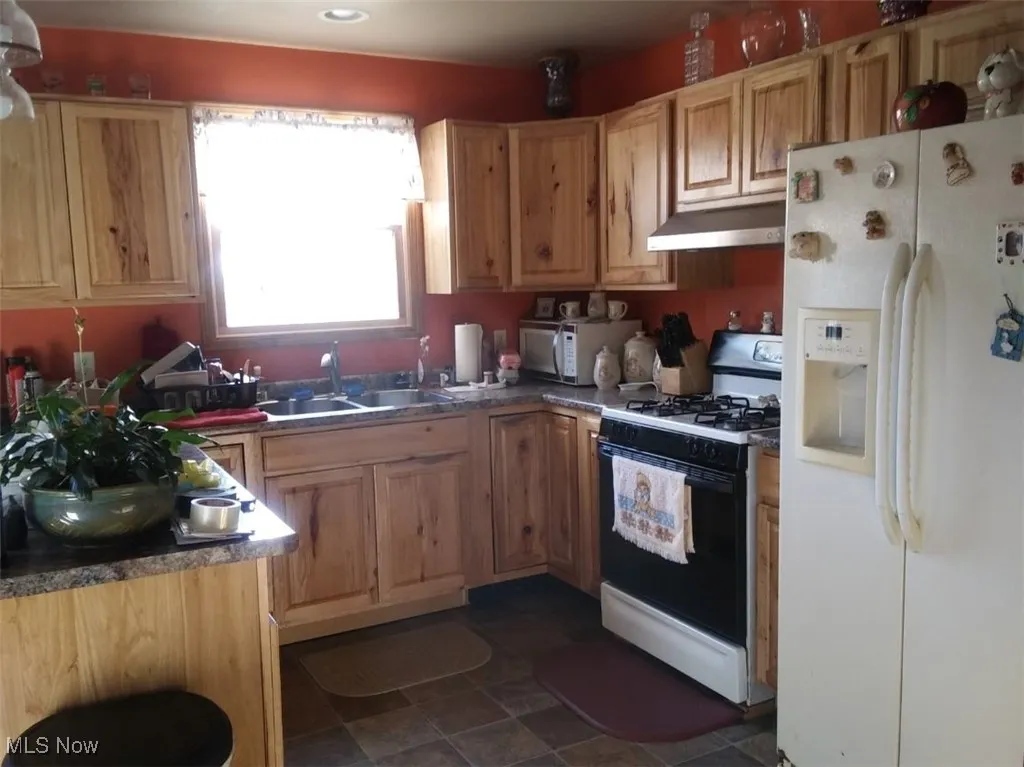 Kitchen featuring under cabinet range hood, a sink, and white appliances