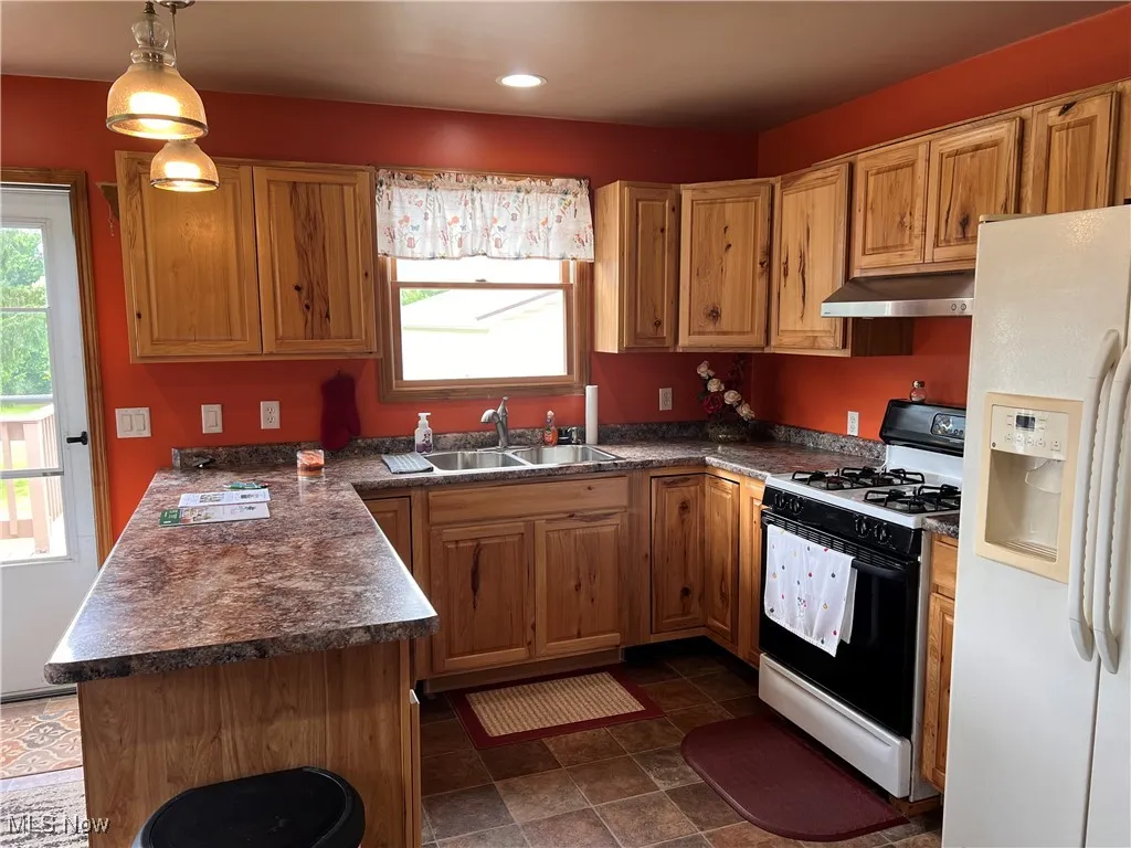 Kitchen featuring white fridge with ice dispenser, range with gas cooktop, under cabinet range hood, dark countertops, and recessed lighting