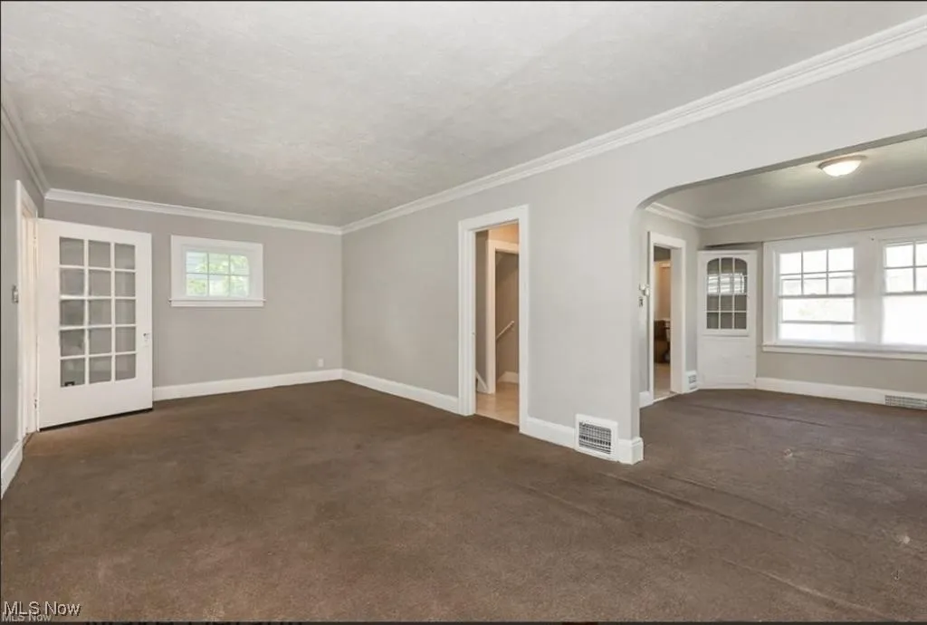 Empty room with baseboards, carpet floors, arched walkways, and visible vents