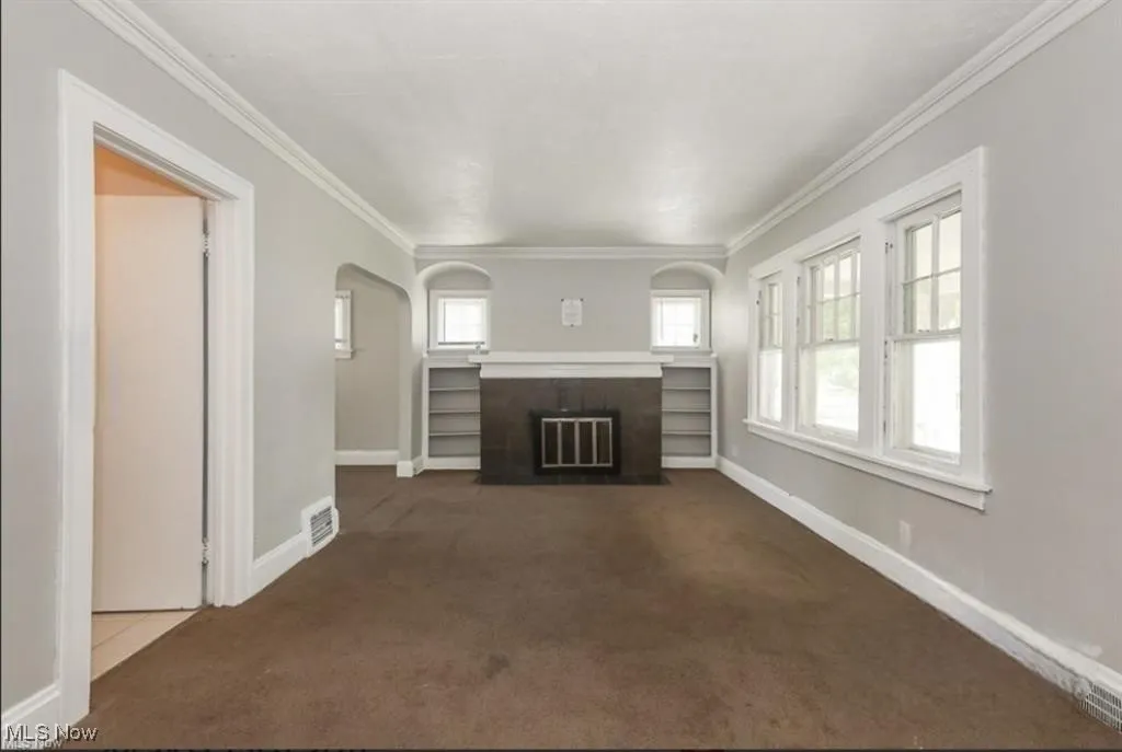Unfurnished living room featuring arched walkways, visible vents, dark carpet, and crown molding