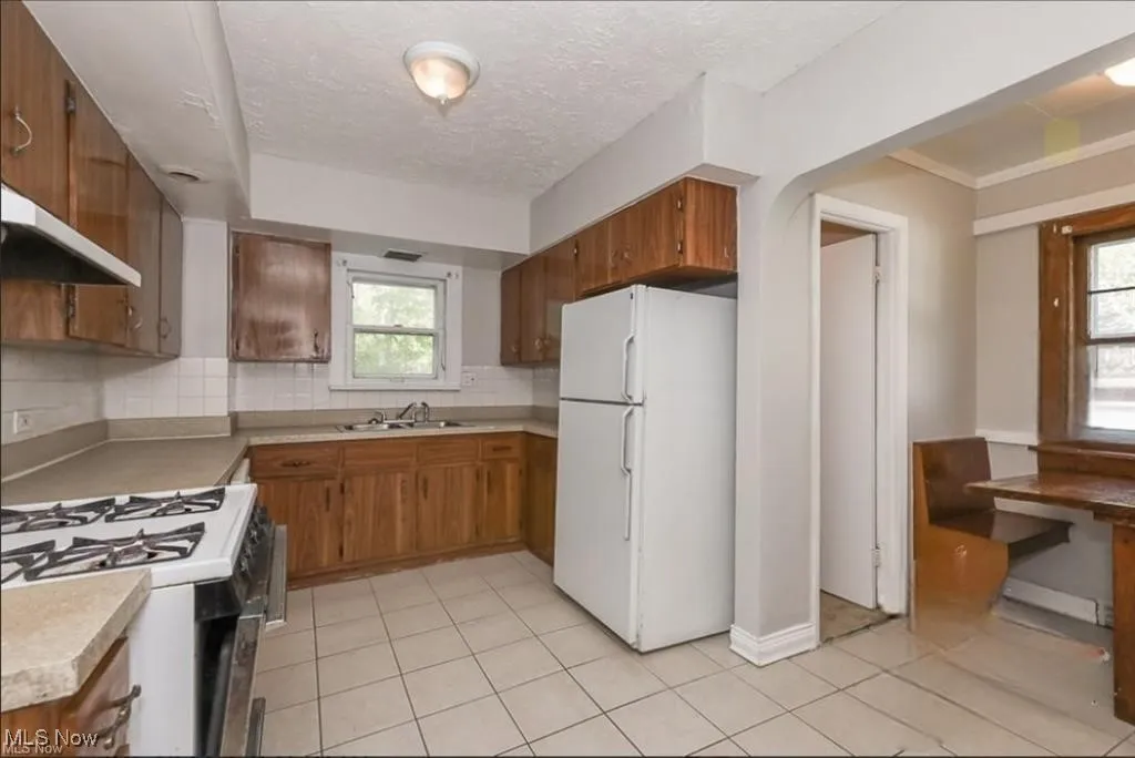 Kitchen featuring light countertops, brown cabinets, a sink, backsplash, and freestanding refrigerator