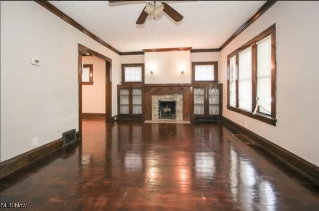 Unfurnished living room with wood finished floors, baseboards, visible vents, ceiling fan, and ornamental molding