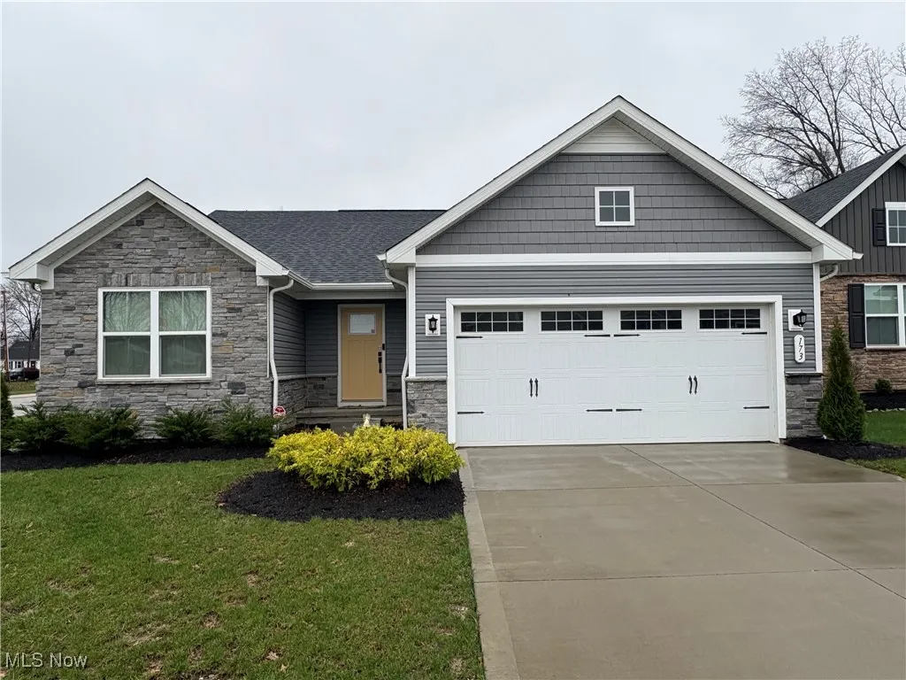 Craftsman-style home featuring stone siding, concrete driveway, a garage, and a front lawn