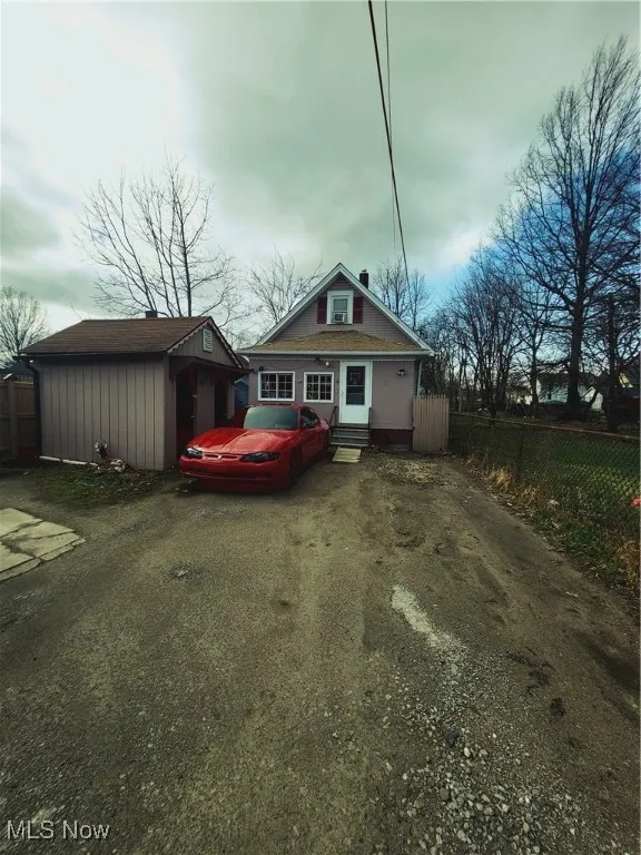 View of front of home with driveway, entry steps, an outdoor structure, and fence