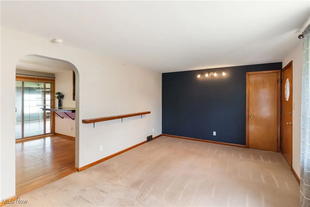 Empty room featuring arched walkways, baseboards, and light carpet