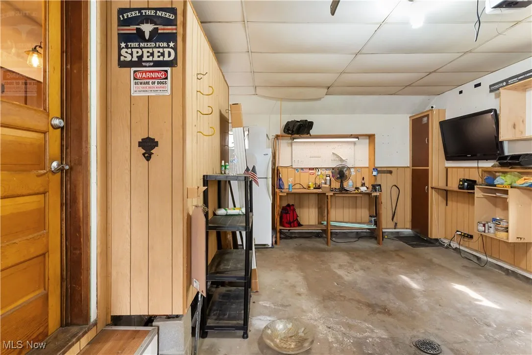 Below grade area featuring a wainscoted wall, wooden walls, freestanding refrigerator, and a drop ceiling