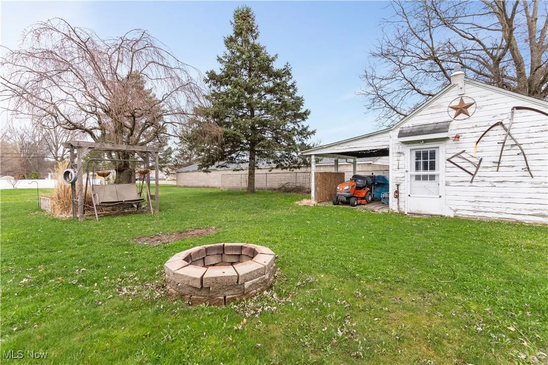 View of yard with an outdoor structure, a fire pit, a carport, and fence