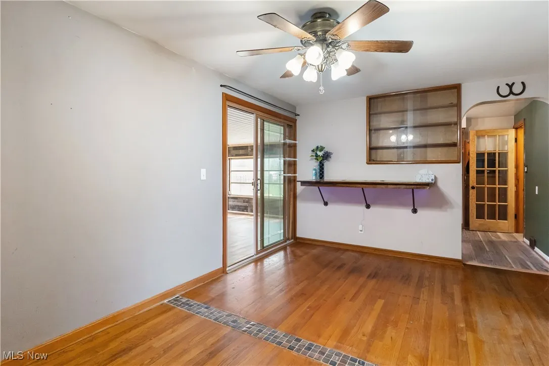 Empty room featuring a ceiling fan, arched walkways, baseboards, and wood finished floors