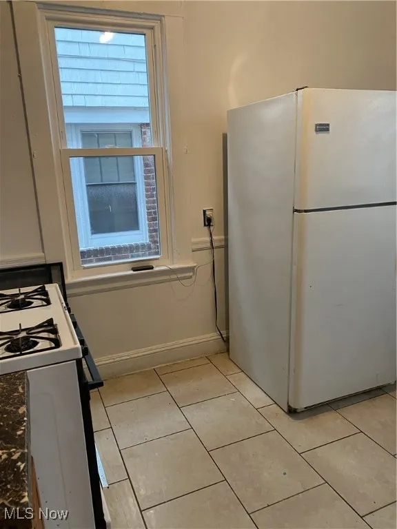 Kitchen featuring fridge, stove, baseboards, and light tile patterned floors