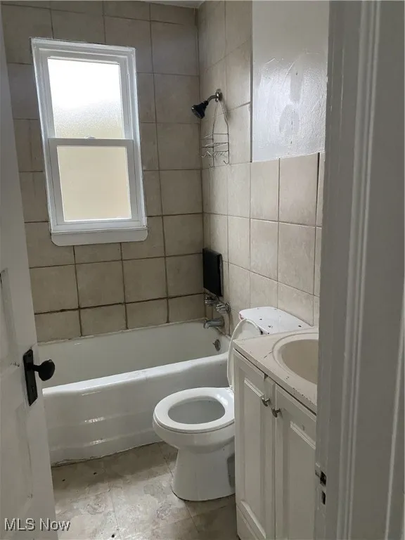 Bathroom featuring shower / washtub combination, toilet, tile walls, and vanity