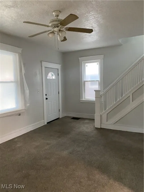 Entryway with dark colored carpet, stairway, baseboards, a textured ceiling, and ceiling fan