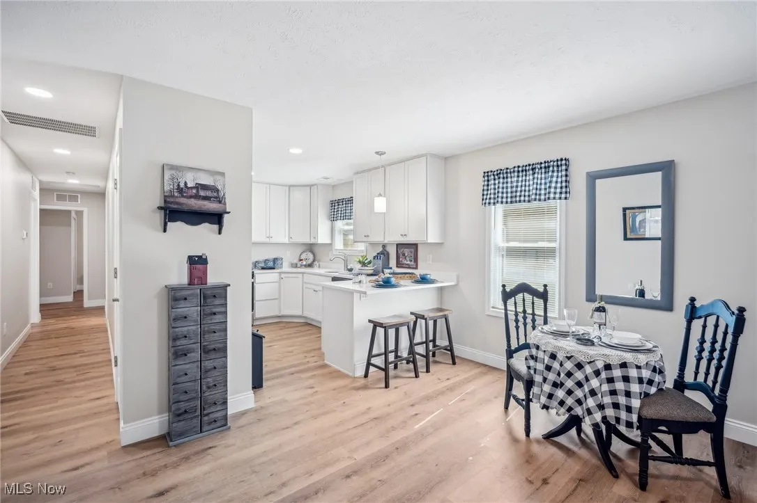 Kitchen featuring visible vents, light wood-style flooring, a kitchen breakfast bar, and white cabinetry