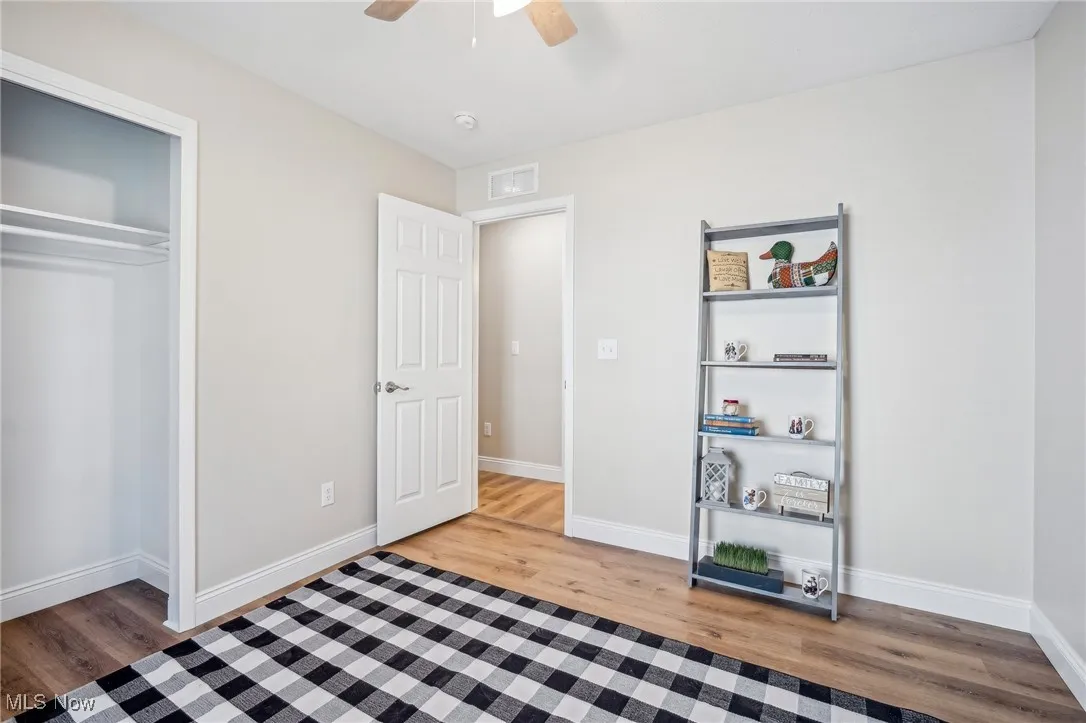 Bedroom with a ceiling fan, visible vents, wood finished floors, baseboards, and a closet