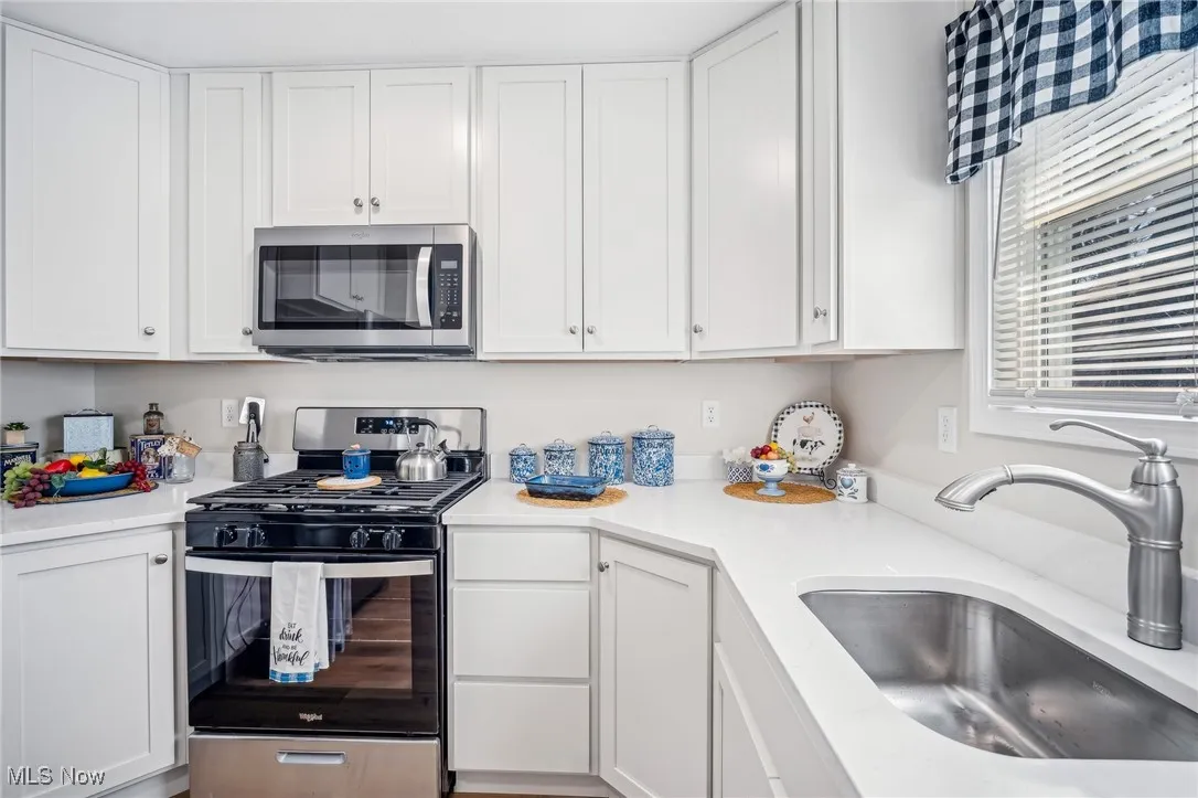 Kitchen with white cabinetry, light countertops, appliances with stainless steel finishes, and a sink