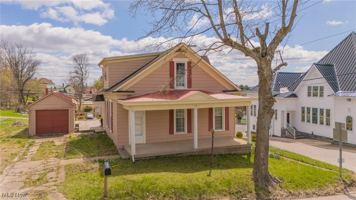 View of front facade featuring covered porch, a detached garage, an outdoor structure, a front yard, and driveway