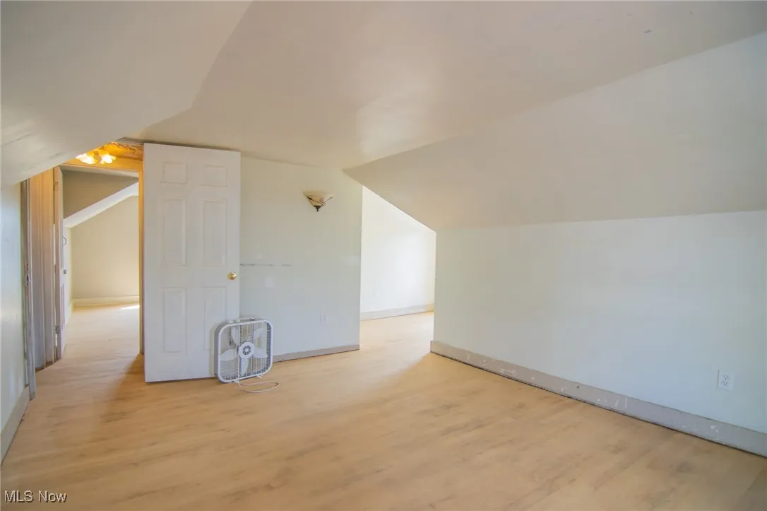 Bonus room with light wood-type flooring, baseboards, and vaulted ceiling