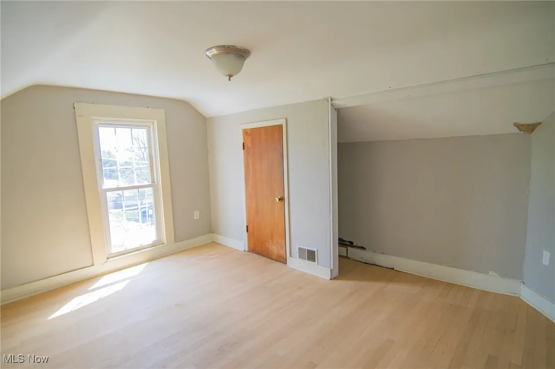 Additional living space with light wood finished floors, visible vents, baseboards, and lofted ceiling