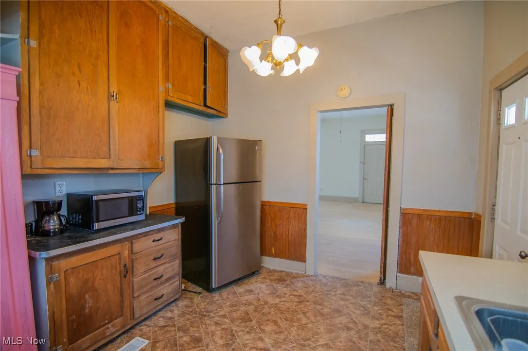 Kitchen featuring an inviting chandelier, brown cabinets, wainscoting, stainless steel appliances, and wood walls