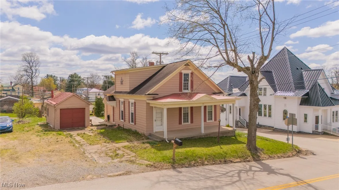 View of front of property featuring an outdoor structure, a chimney, a detached garage, dirt driveway, and covered porch
