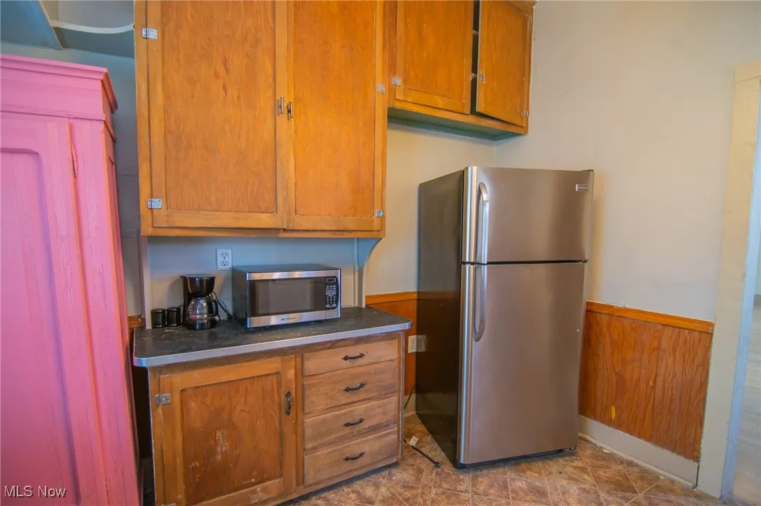 Kitchen with dark countertops, wood walls, wainscoting, brown cabinetry, and stainless steel appliances