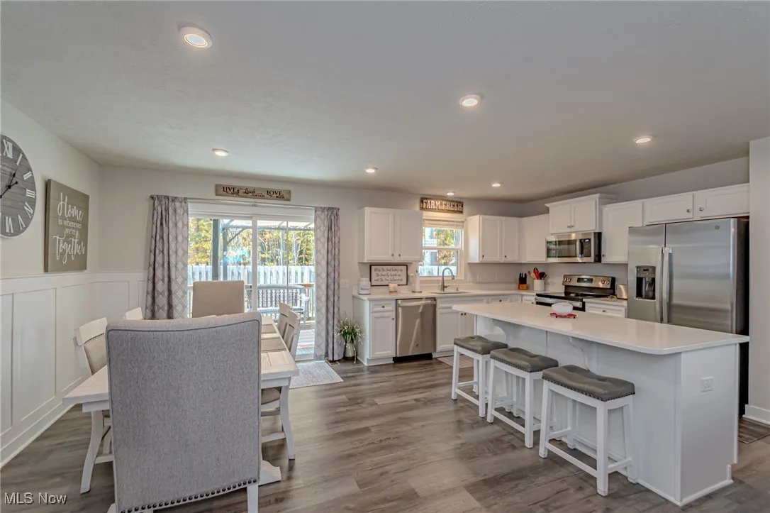 Kitchen featuring a center island, a sink, appliances with stainless steel finishes, dark wood-style floors, and white cabinetry