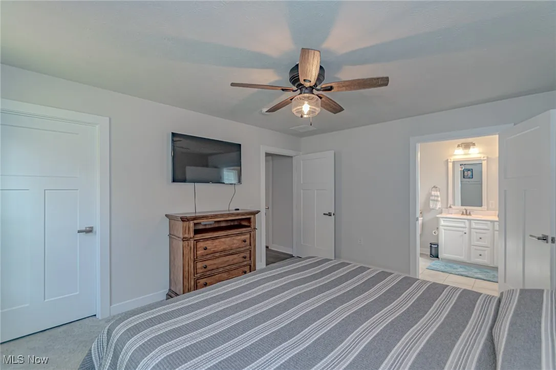 Bedroom featuring baseboards, a sink, a ceiling fan, connected bathroom, and light carpet
