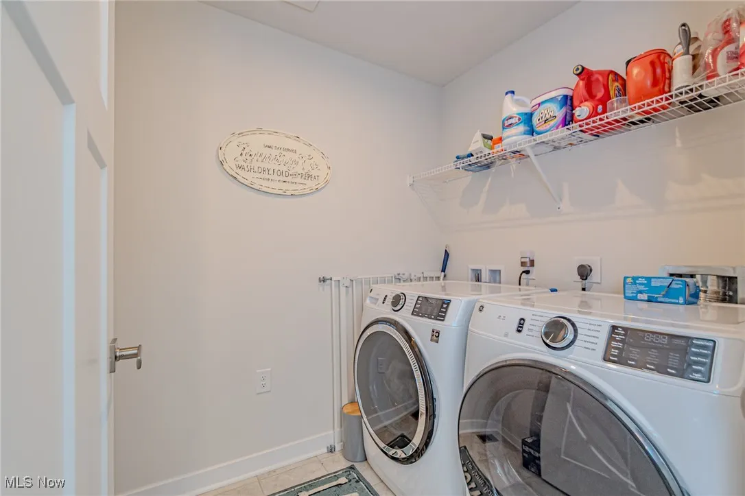 Washroom featuring laundry area, separate washer and dryer, light tile patterned flooring, and baseboards