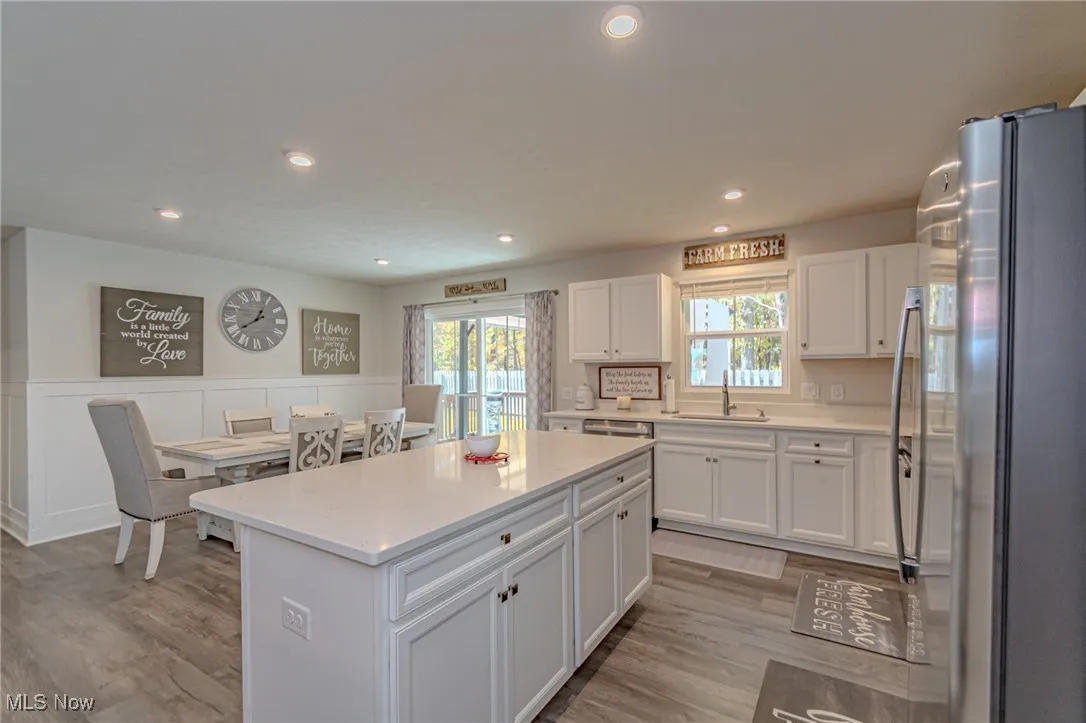 Kitchen featuring light wood-style floors, freestanding refrigerator, white cabinetry, a wainscoted wall, and a sink