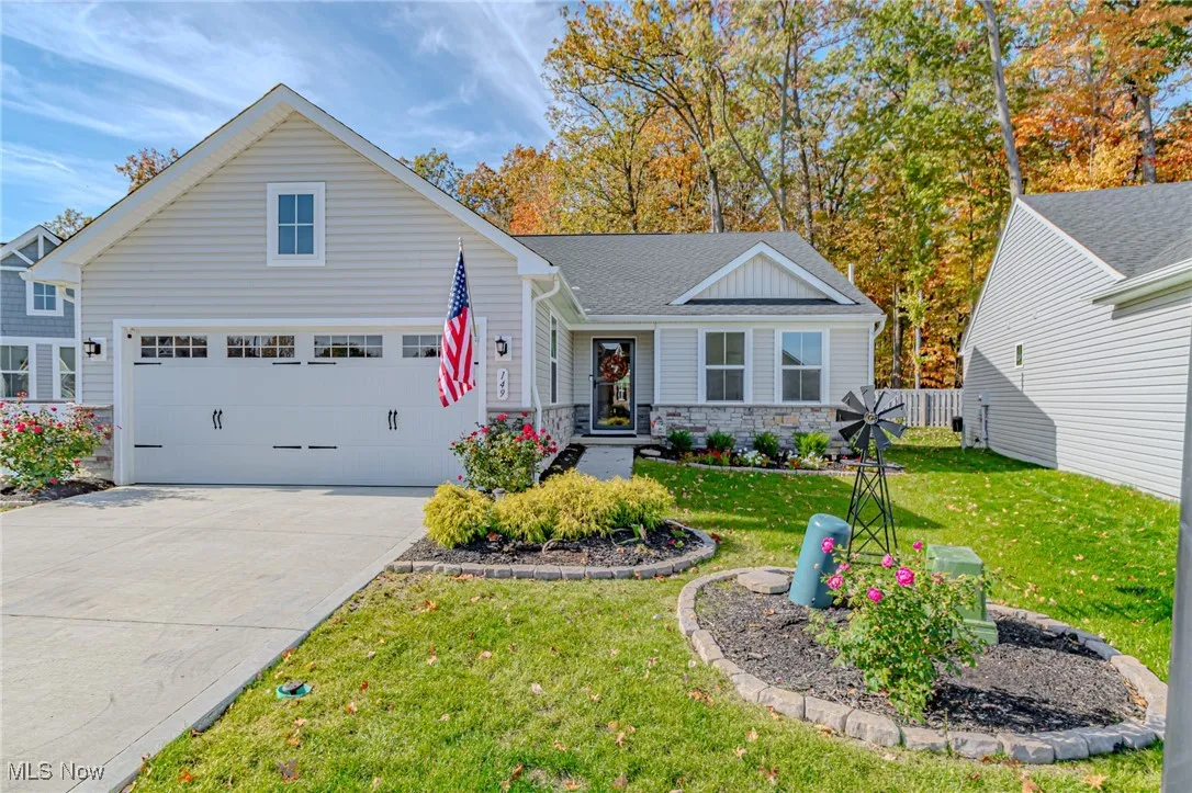 Ranch-style house featuring an attached garage, stone siding, a front lawn, driveway, and roof with shingles