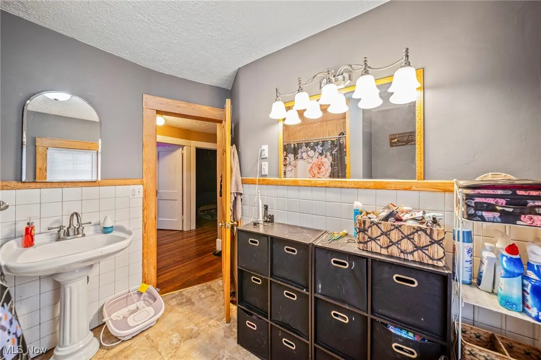 Bathroom featuring a sink, tile walls, wainscoting, and a textured ceiling