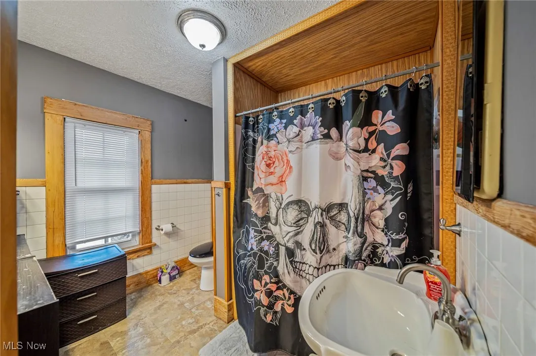 Full bathroom featuring a shower with shower curtain, a sink, tile walls, a textured ceiling, and a wainscoted wall