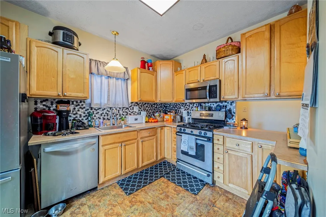 Kitchen with pendant lighting, light countertops, a sink, stainless steel appliances, and decorative backsplash