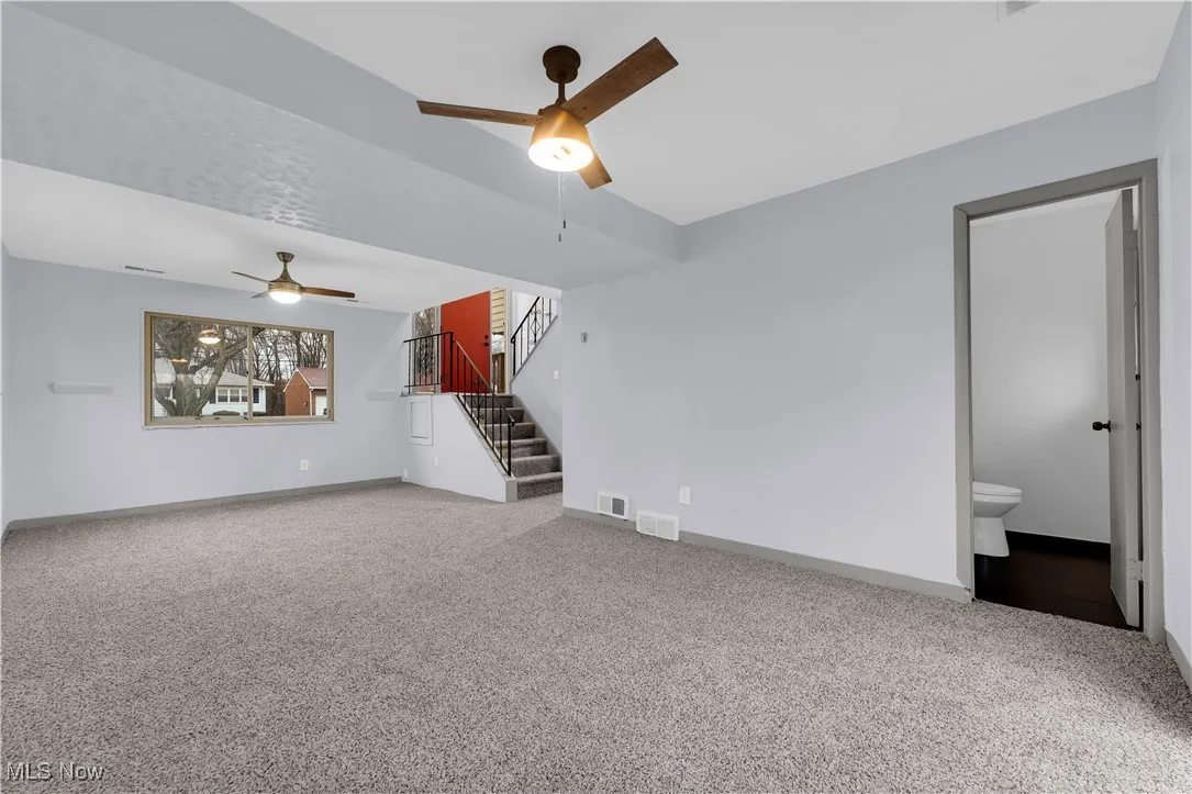 Unfurnished living room with ceiling fan, visible vents, stairway, carpet floors, and baseboards